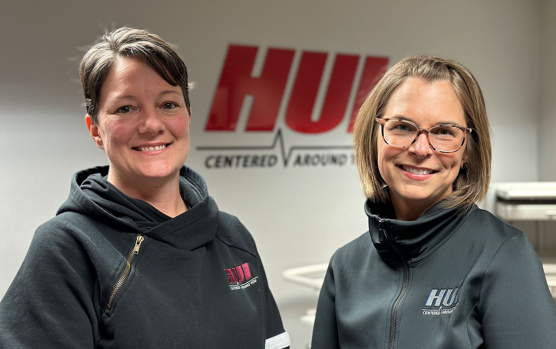 two females smiling in front of HUI manufacturing signage